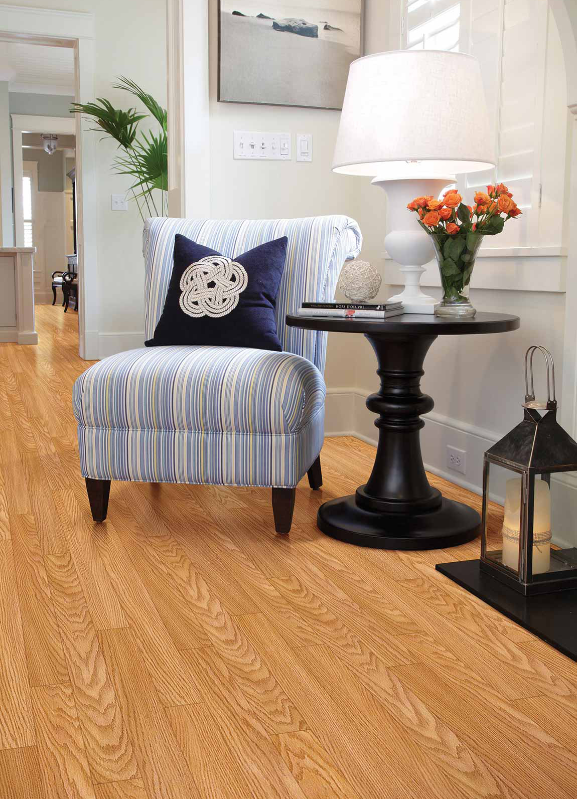 Laminate flooring by Shaw Floors. Wood-look laminate in hallway featuring end table, lamp, and blue armchair.